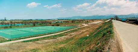 重なる山並みが望め、清流のそばのテニスコート